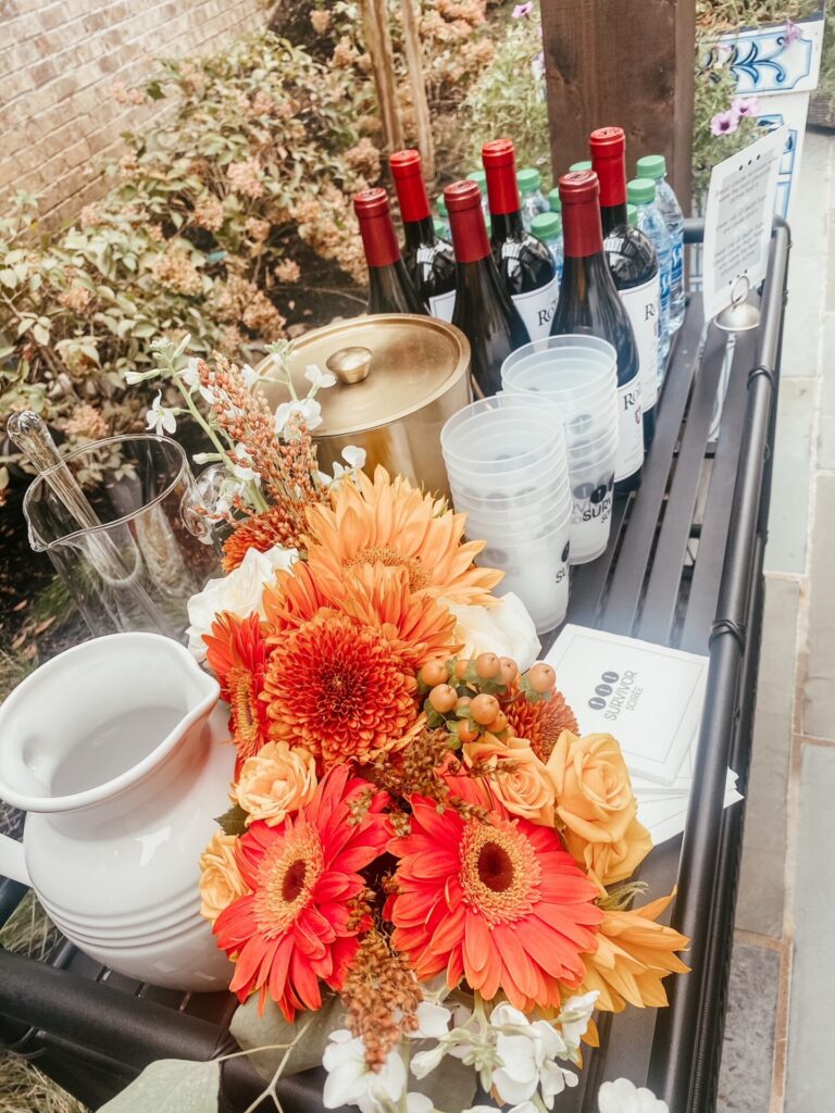 Dinner Party Ideas by popular Nashville lifestyle blog, Hello Happiness: image of a black bar cart set up with a orange flower arrangement, wine bottles, water bottles, gold ice bucket, and white pitcher.   
