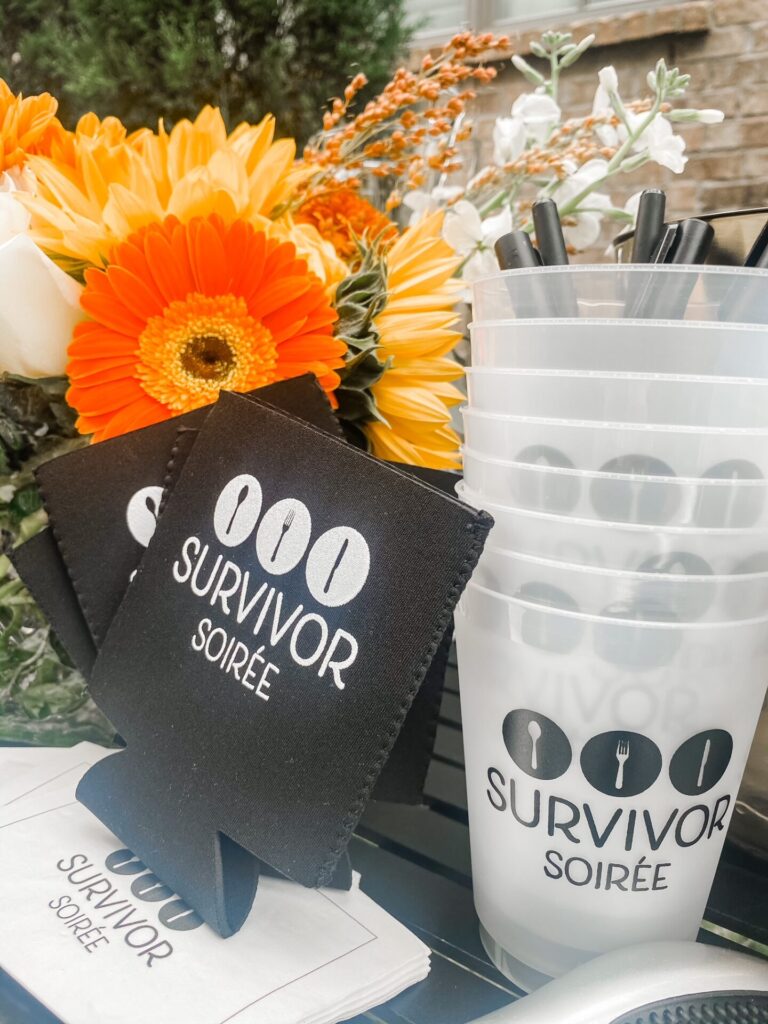 Dinner Party Ideas by popular Nashville lifestyle blog, Hello Happiness: image of a table set with Survivor Soiree cozies, Survivor Soiree plastic drink cups, and a orange flower arrangement.  
