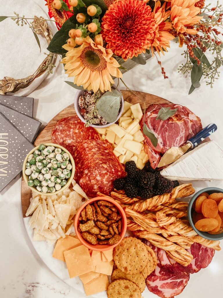 Dinner Party Ideas by popular Nashville lifestyle blog, Hello Happiness: image of a table set with orange flower arrangements and a charcuterie board. 