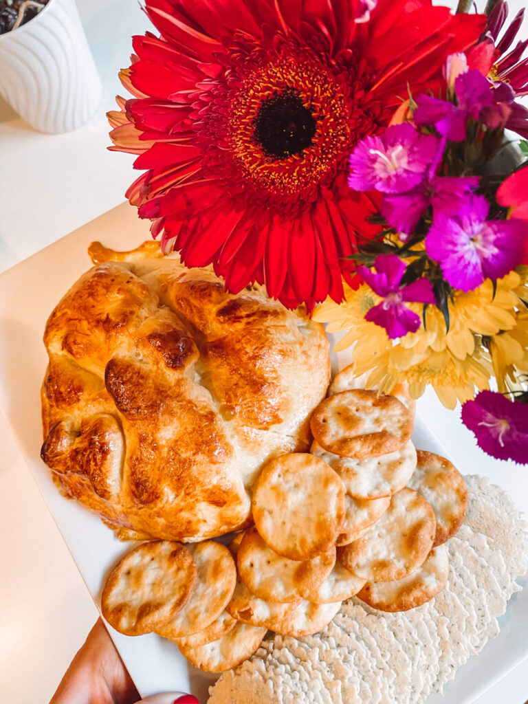 Baked Brie Recipe by popular Nashville lifestyle blog, Hello Happiness: image of baked brie and crackers on a white plate next to a red gerber daisy flower arrangement. 