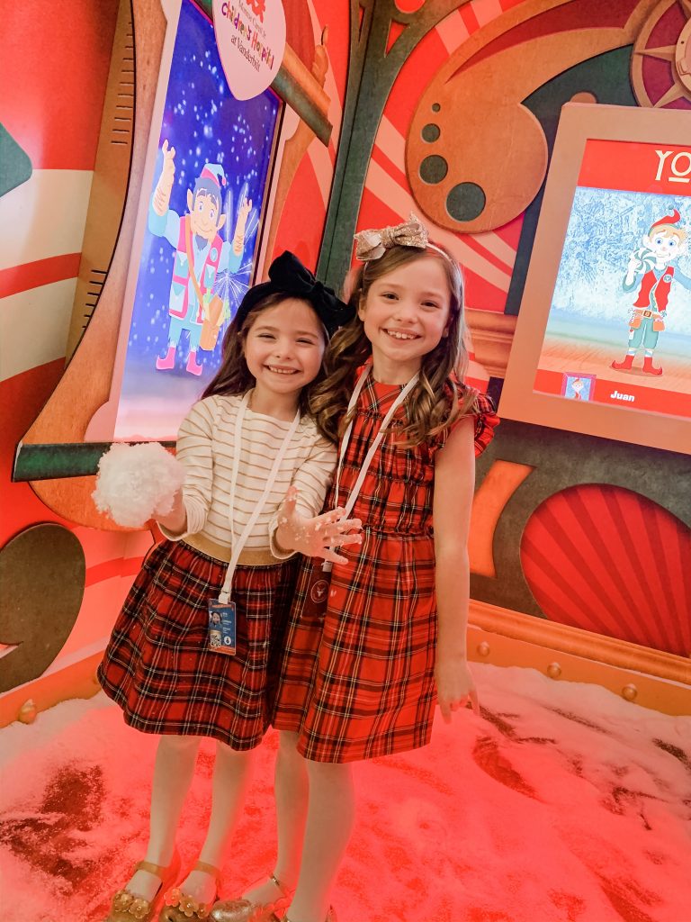 All Our Favorite Family Holiday Traditions by popular life and style blog, Hello Happiness: image of two girls at Santa's flight academy and wearing J. Crew Girls' smocked flutter-sleeve dress in red Stewart tartan, Amazon mini melissa Kids' Mini Ultragirl Special Ballet Flat, J. Crew Girls' velvet bow headband, and J. Crew Girls mixy dress in Stewart tartan.