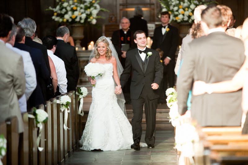 10 Year Wedding Anniversary by popular Nashville lifestyle blog, Hello Happiness: image of a bride wearing a strapless lace wedding dress and holding a white floral bouquet and a groom wearing a black tuxedo and holding hands as they walk down the aisle inside a cathedral. 