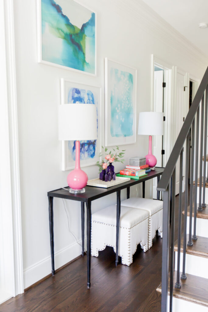 Home Paint Colors by popular Nashville life and style blog, Hello Happiness: image of a front entry way with framed original Greg Irby artwork, pink lamps, and white leather studded stools. 
