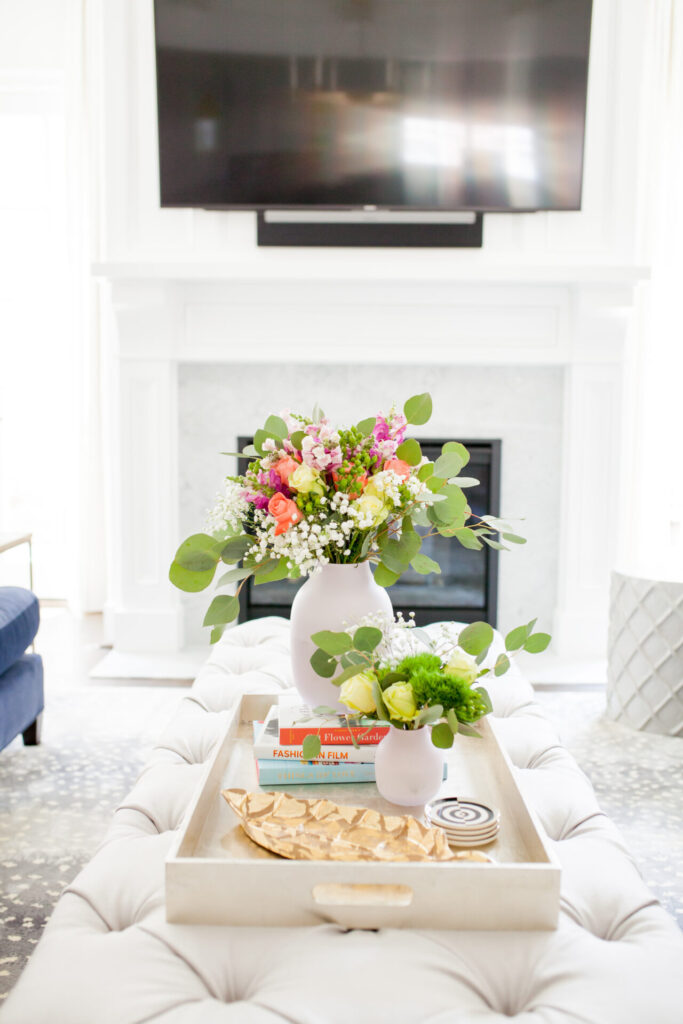 Coffee Table Books by popular Nashville lifestyle blog, Hello Happiness: image of a stack of coffee table books inside a white wood tray resting on a white tufted ottoman. 
