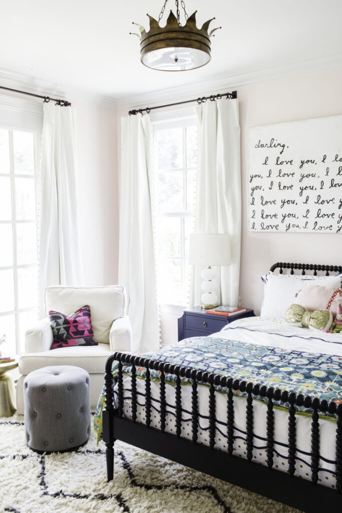 Home Paint Colors by popular Nashville life and style blog, Hello Happiness: image of a little girl's room with a crown pendant light, black jenny lind bed, and walls painted in Benjamin Moore Frosty Pink.