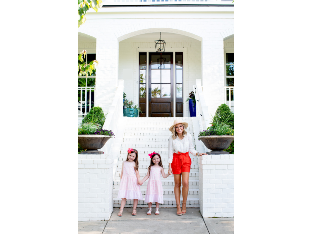 Home Paint Colors by popular Nashville life and style blog, Hello Happiness: image of a mom and her two daughters standing in front of their white brick house. 