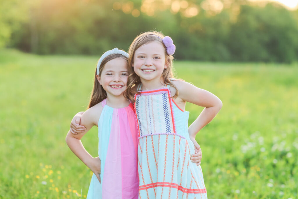 Summer Bucket List by popular Nashville lifestyle blog, Hello Happiness: image of two girls embracing each other in a grassy meadow and wearing Matilda Jane Clothing dresses. 