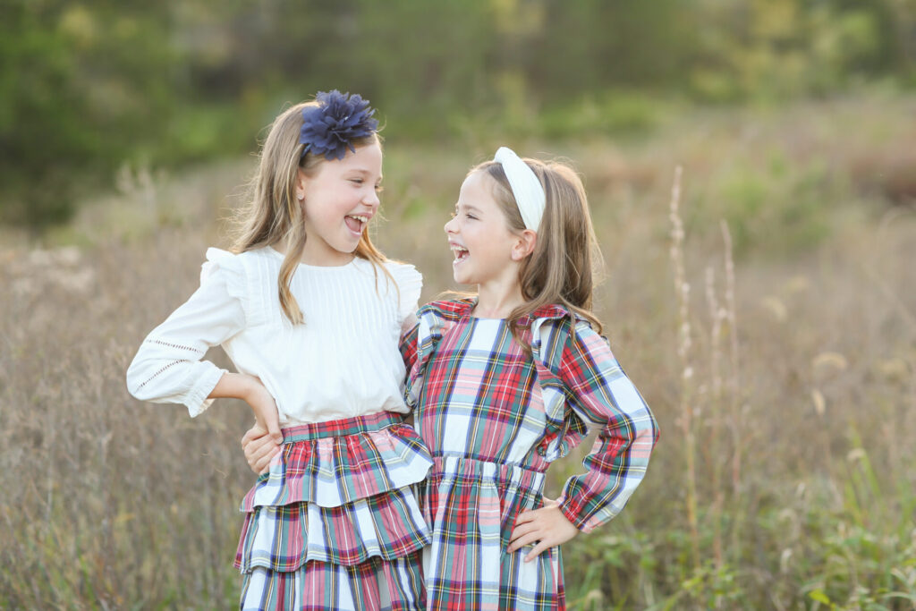 Gift Ideas for Girls by poplar Nashville life and style blog, Hello Happiness: image of two young girls standing next to each other in a field and wearing a white blouse, gold ballet flats, blue sandals, blue flower headband, white knot head band, plaid tier skirt, and plaid dress. 